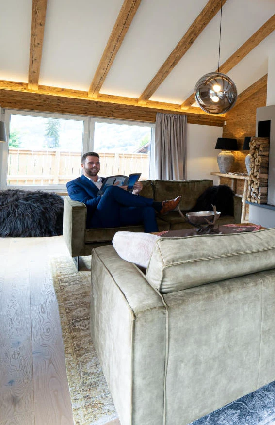 Sandro Anibas sitzt in einer luxuriösen Wohnung und schaut lächelnt von einer Zeitschrift auf